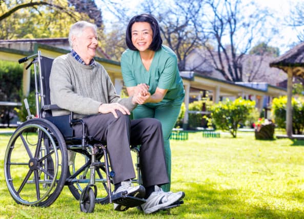 elderly in a wheelchair holding hands with caregiver and smiling